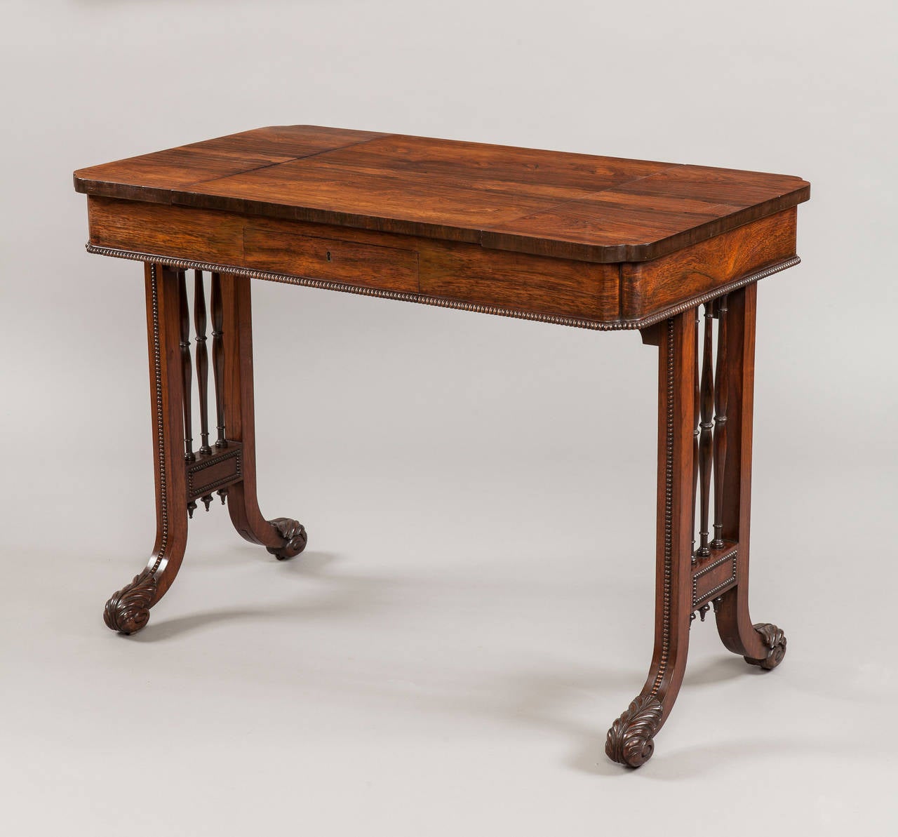 Constructed in a finely figured goncalo alves; the end supports having square uprights, each enclosing three tapering and turned ‘triple spindles’, with ‘running pearl’ adornments, and terminating in incurving carved scroll toes; the platform having