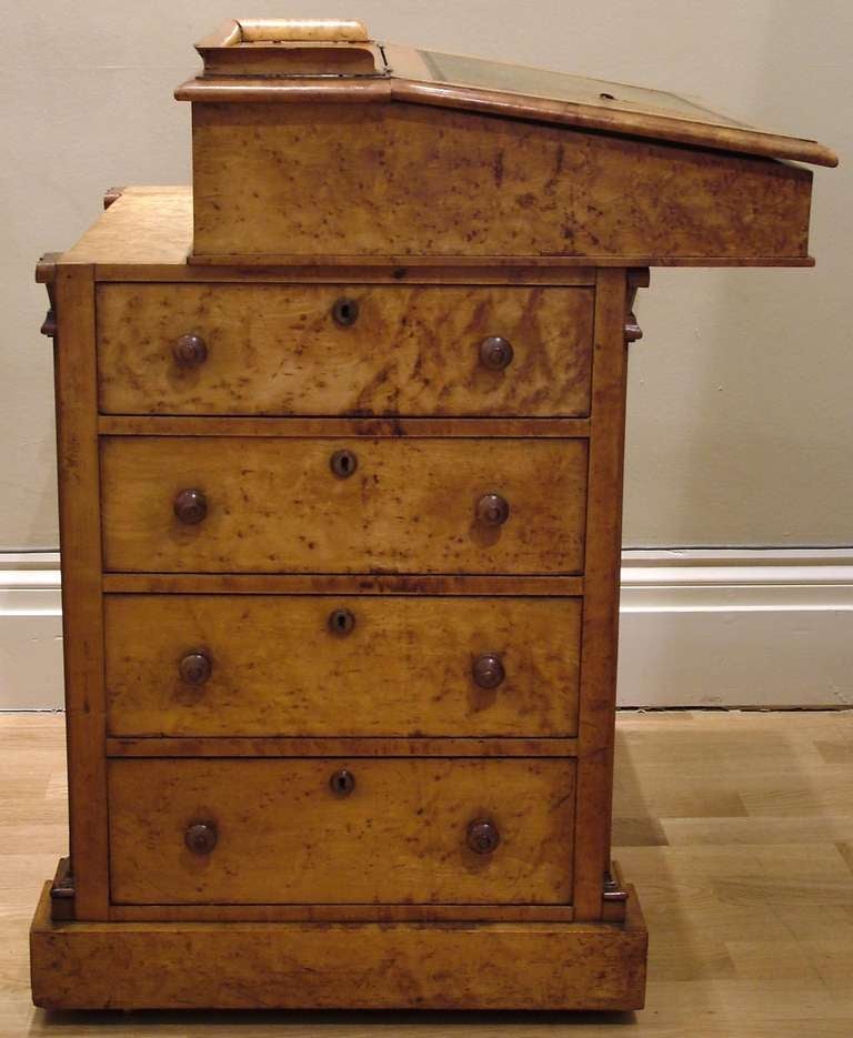 Constructed in a finely figured and patinated Maple; rising from a plinth base, incorporating four graduated drawers to the side, with turned wood knobs; the other three sides of fielded panel type, with a slide action writing cabinet having a