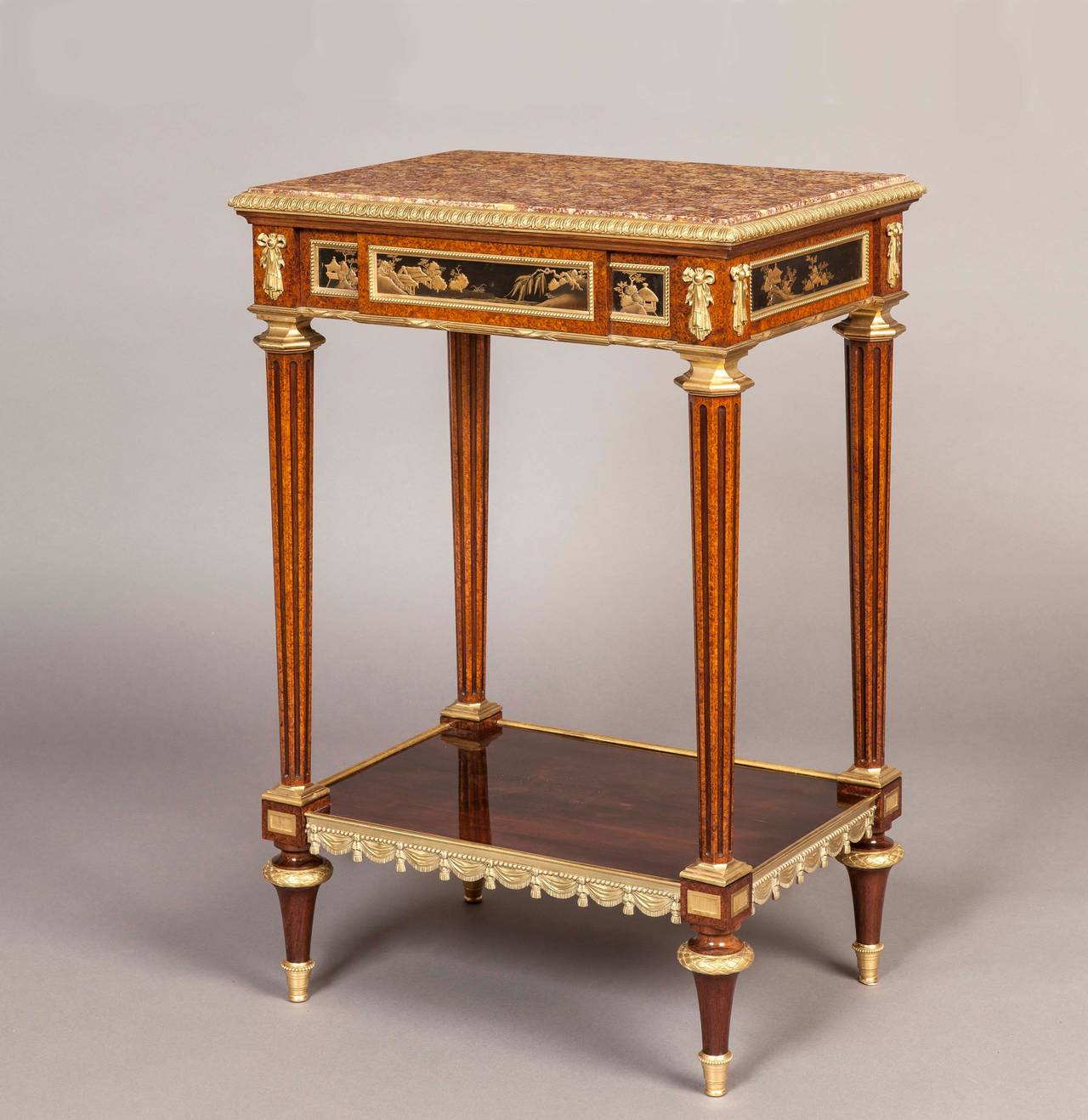 Of rectangular form, constructed in amboyna and mahogany dressed with chinoiserie panels, and fine ormolu mounts; rising from ormolu mounted toupie feet, supporting the lower platform, itself adorned with running swags; the fluted tapering legs