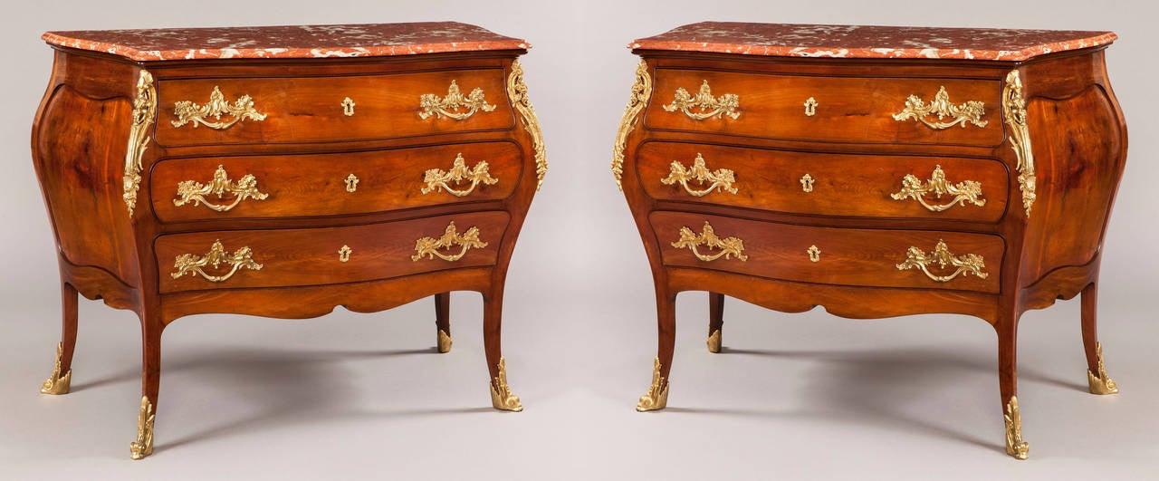 A pair of French commodes in the Louis XV manner.

Constructed in mahogany, dressed with gilt bronze mounts and having Languedoc rouge marble platforms; rising from swept cabriole legs, mounted with scrolled gilt bronze toes and foliate