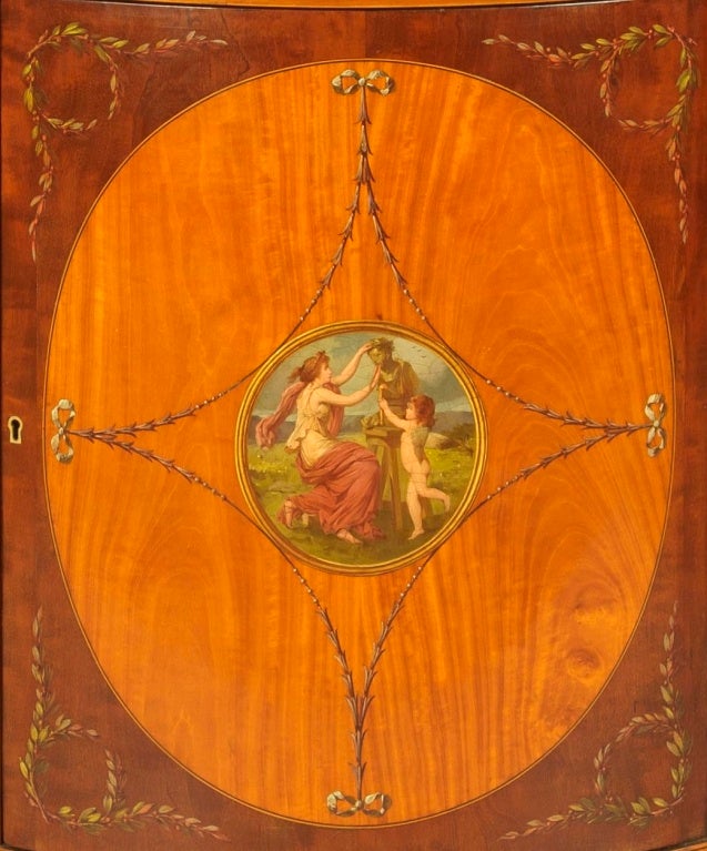 Fine side cabinet in the Adams Manner

Constructed in finely figured satinwood and mahogany of great depth of colour, with polychrome hand painted decoration in the style of Angelica Kauffman and Pergolesi; of arc-en-arbalette form, rising from