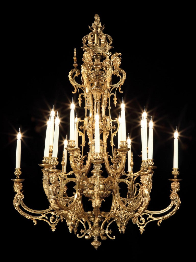 Constructed in gilt bronze, having twelve scrolled arms, of alternate paired and single candle holders, of ‘S’ form, depicting male herms projecting the candle holders, issuing from a shaped central column, terminating in berries below, with a
