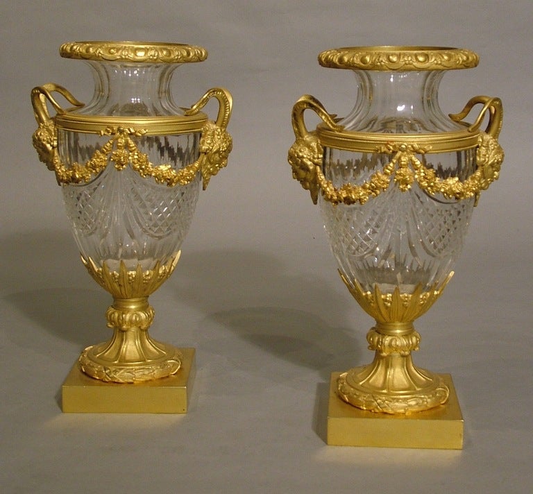 A Good Pair of Mantle Urns in the Louis XVIth Manner

Constructed in cut lead crystal glass, and gilt bronze: rising from square form bases, the bronze socles, displaying foliates and cannellures, support baluster form urns with everted rims,