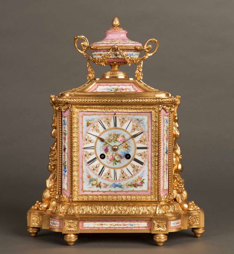A Good Mantle Clock in the Louis XVI Manner 

Constructed in ormolu and adorned with ‘jewelled’ Sevres style hand decorated porcelain with a rose ground; the eight day silk suspension movement, having the hours striking on a bell is housed with a