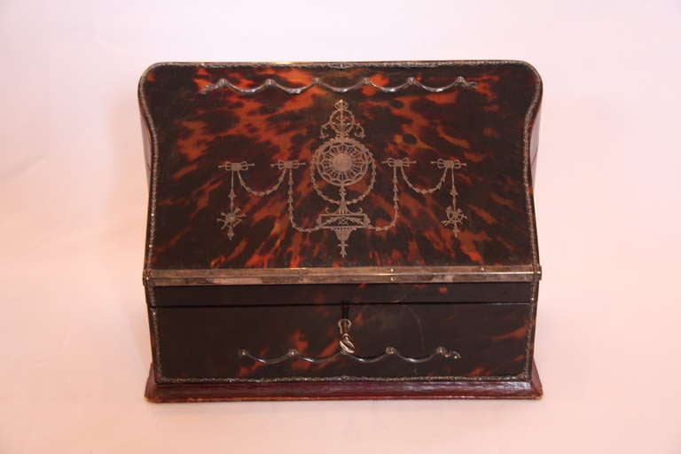 Two silver and glass inkwells on a tortoiseshell stand with accompanying letter rack and lid. The letter rack has a slant oblong front opening to a silk slotted interior, the sides and and back in red 
Morocco leather with classical decoration.