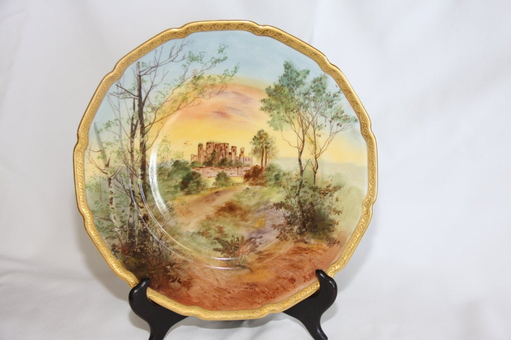 Set of twelve English painted porcelain cabinet plates made by Royal Doulton and retailed by Ovington's, early 20th century. The scalloped, gilt-tooled rim encloses assorted painted landscape scenes. Marked titled in underglaze on the underside. The