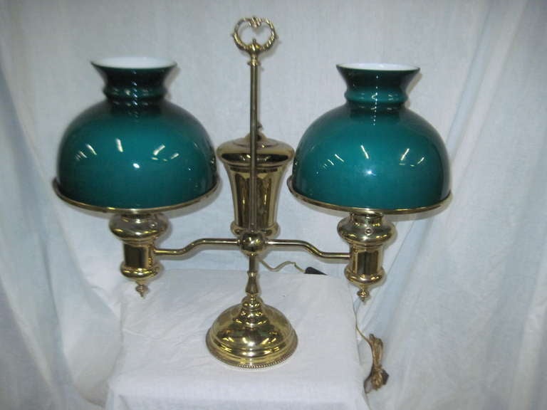 Rare and desirable dual student lamp. New old stock matched set of a very pretty deep teal blue green glass shades with white  lining. High polish brass. Marked John Wannamaker on burner valves. Weighted base, adjustable armature.
