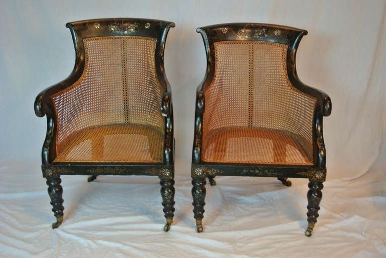 Handsome pair of antique armchairs with great silhouette. These chairs are of a black painted hardwood with mother of pearl inlay. The hand painted trim of flora and fauna. These chairs have good old rattan seating with upholstered cushions that fit