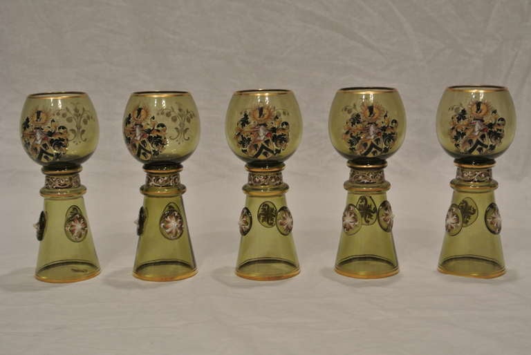 Set of 5 green wine glasses with painted crest and floral motif. Each with a green glass bowl molded with leafage on faceted stem and circular green glass base.