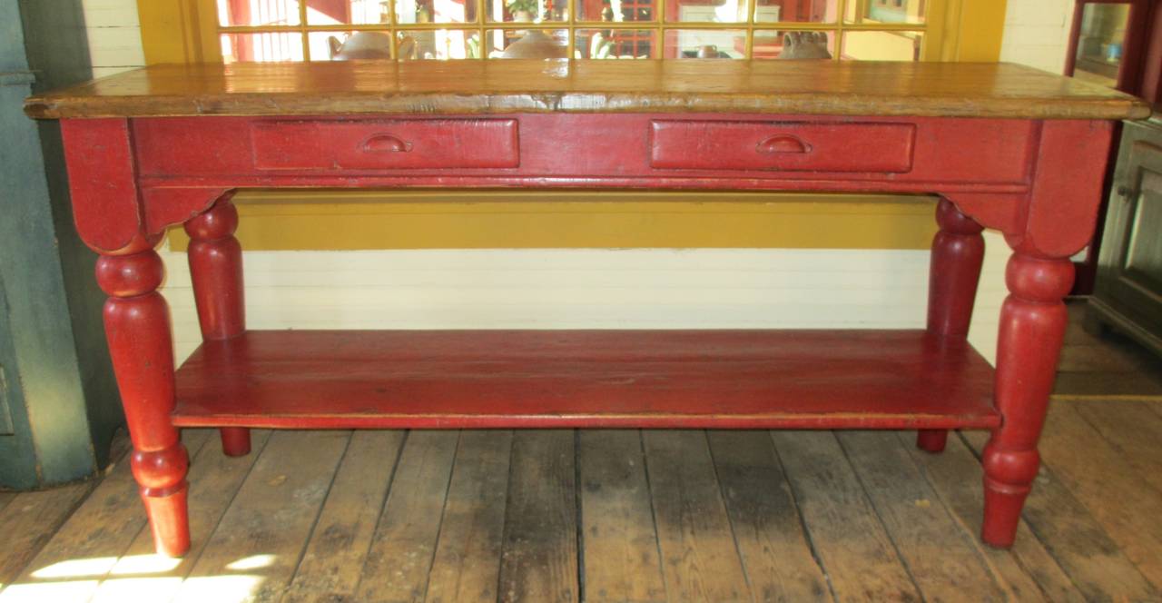 A red counter with lower open shelf, turned legs, two drawers.