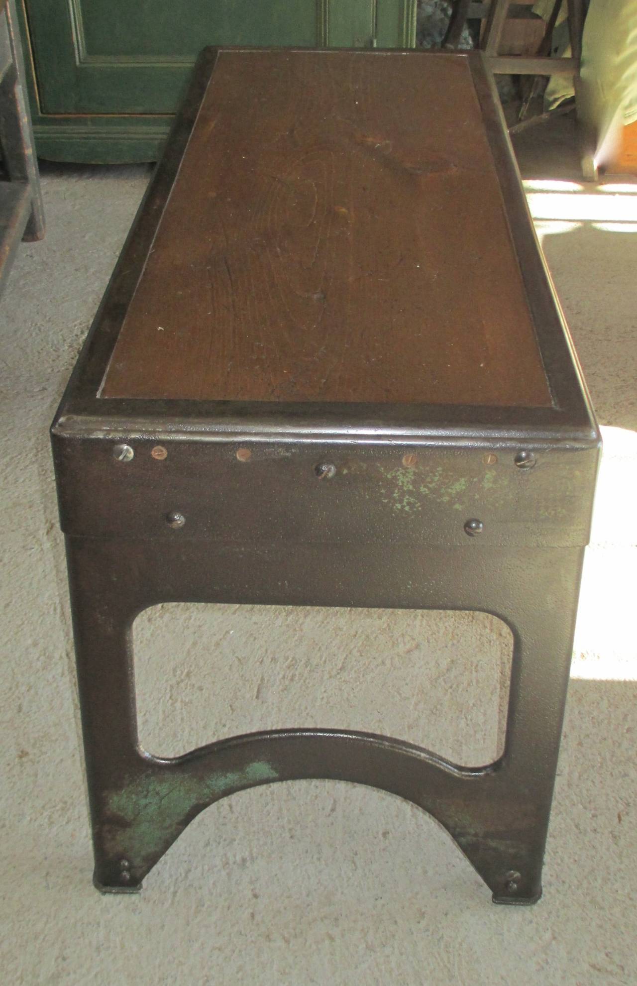 A small workshop bench. A metal green patina base with a wooden top.
