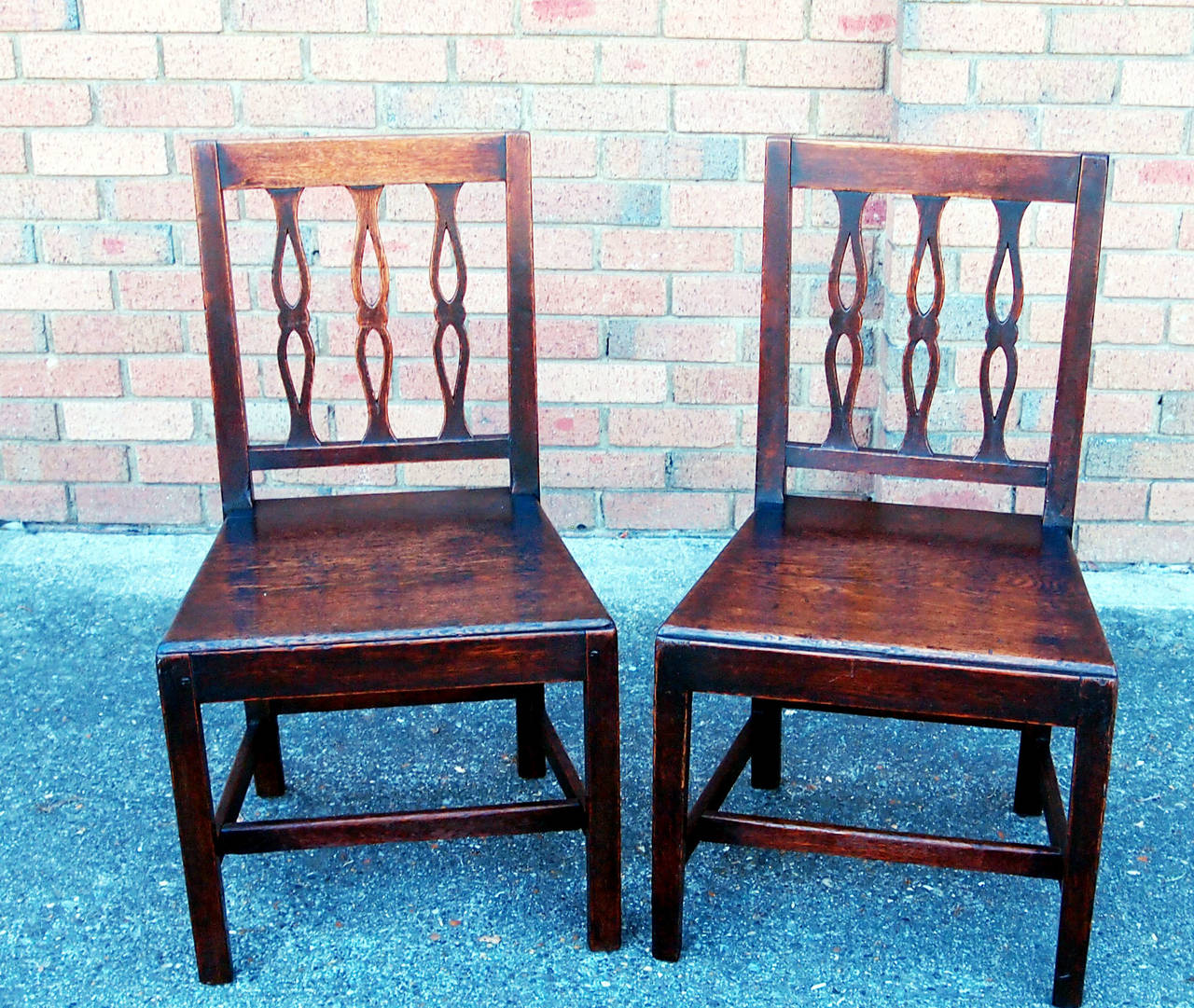 An attractive set of six 18th century
oak dining chairs having unusual shaped
and pierced vertical ladder backs above
panelled seats raised on square legs and stretchers.