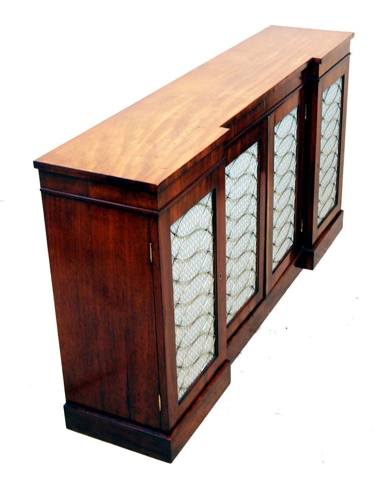 A Superb Quality Regency Period Mahogany Inverted Breakfront 
Side Cabinet Having Superbly Figured Top Above Four Brass 
Grilled And Upholstered Panel Doors Enclosing Shelves Raised On 
Original Plinth Base