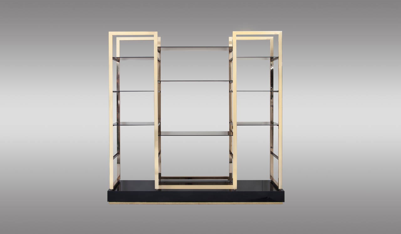 Pair of etageres in solid gold plated steel structure with smoked glass shelves. Sit atop black laminated base finished on brass. In the manner of Romeo Rega. 1970 (Can be sold separately)