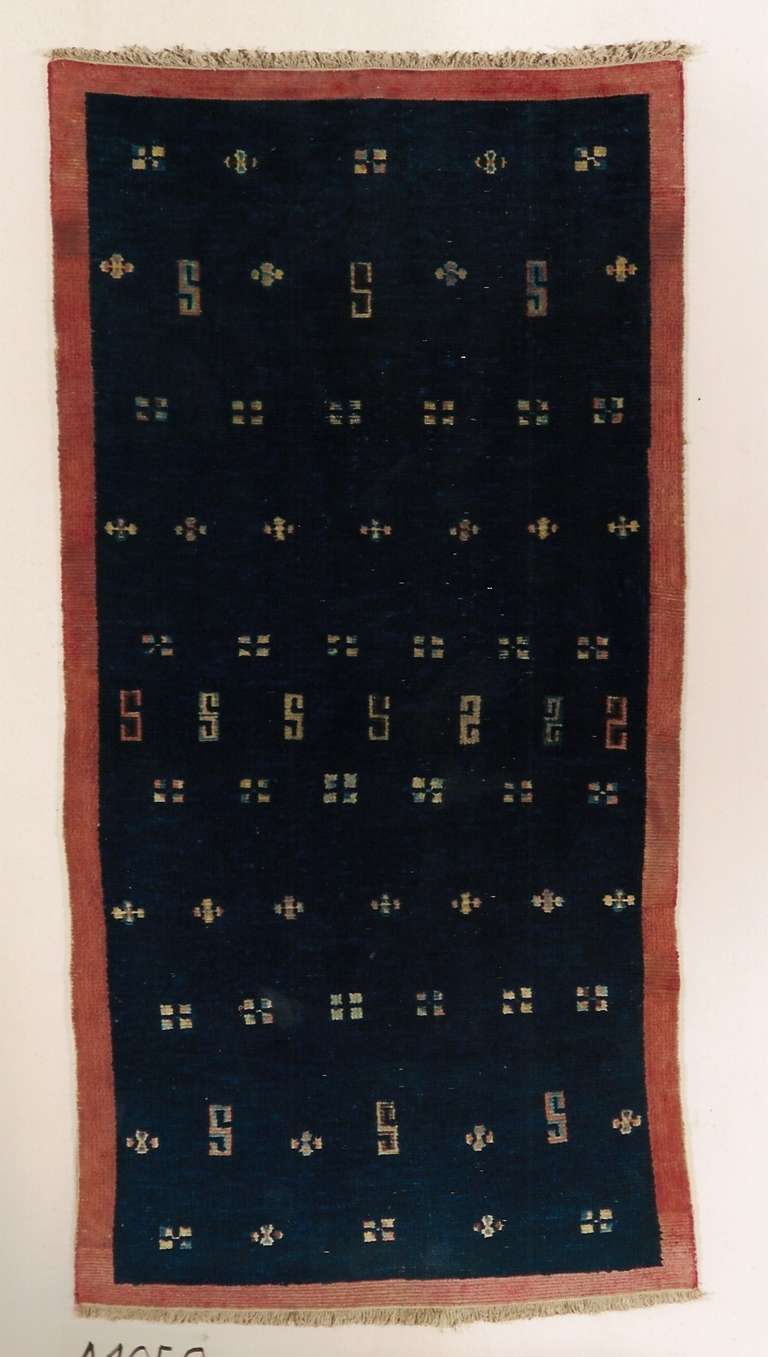 Small Khaden (rug to sleep on) recalling a “Tsuk-Truk “(blanket or mantel), with a light deep indigo field and red frame, as “Tsuk-Truk” used to have a felt red border. The filed shows symmetric narrows Tibetan sacred signs, intended as homage to