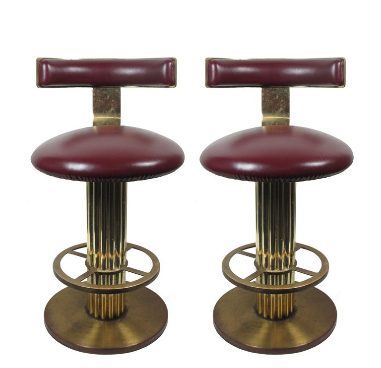 A pair of brass plated barstools with a reeded column and upholstered swivel seat and back. In original burgundy naugahyde upholstery.  Presently in un-restored condition.