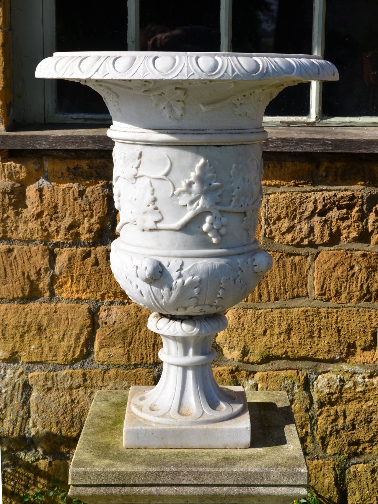 The main body of the urn having vine and grape embellishment, this pattern continuing under the rim with the top of the rim being carved with an egg and dart motif. The urn base has acanthus leaf decoration raised upon a fluted socle.