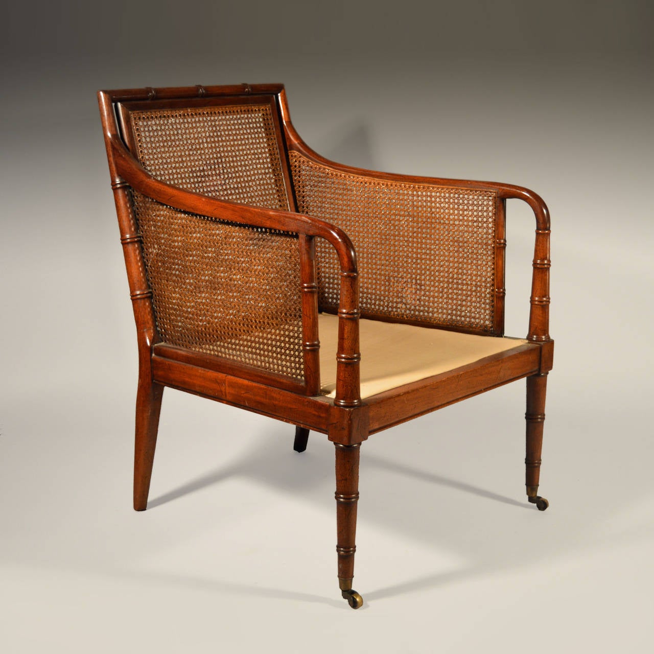 An early 20th century mahogany library chair with bamboo simulated frame, with deep seat and legs terminating in brass castors.
