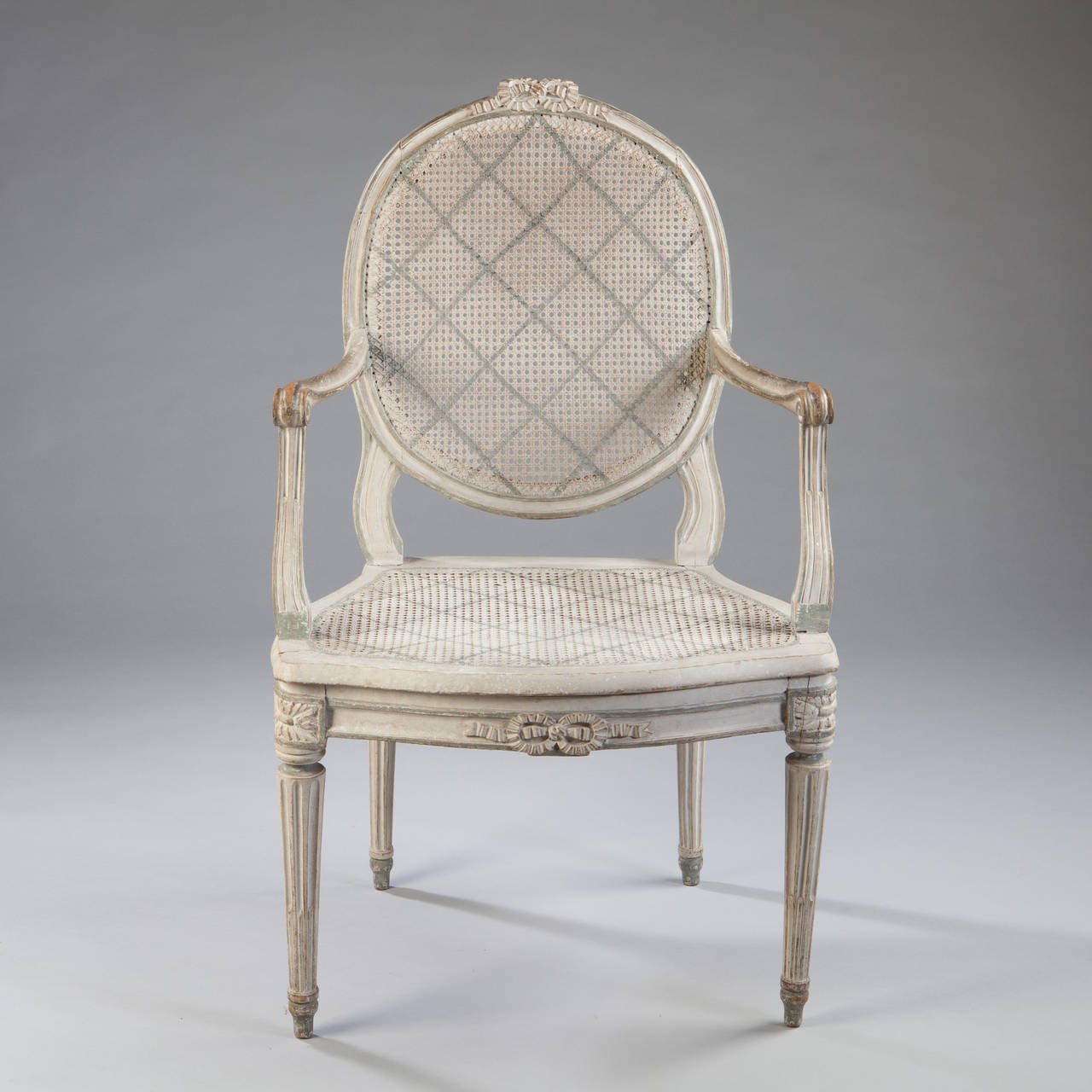 A fine pair of mid 18th century painted open arm chairs with oval frames surmounted by a bow, the backs and seats caned all supported on fluted tapering legs.