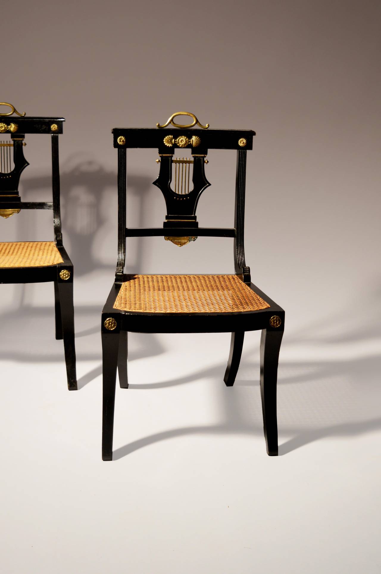 A pair of late 19th century ebonised side chairs with brass mounts and caned seats in the Greek taste.
