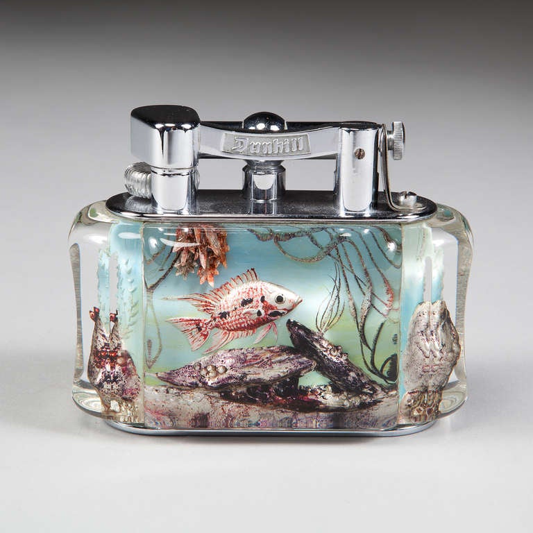 A very fine collection of three Dunhill Aquarium Table Lighters 

Each with raisable arms stamped Dunhill, above the lucite body carved with fish on the front and back. The scenes are all well composed and colourful, the fish are well proportioned