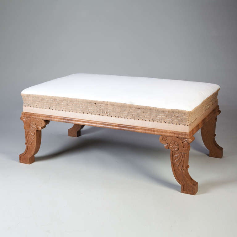 A carved oak stool raised on four curved legs with anthemion palmettes and scrolls after Regency period designs by Thomas Hope, the legs supporting an large upholstered seat. 


