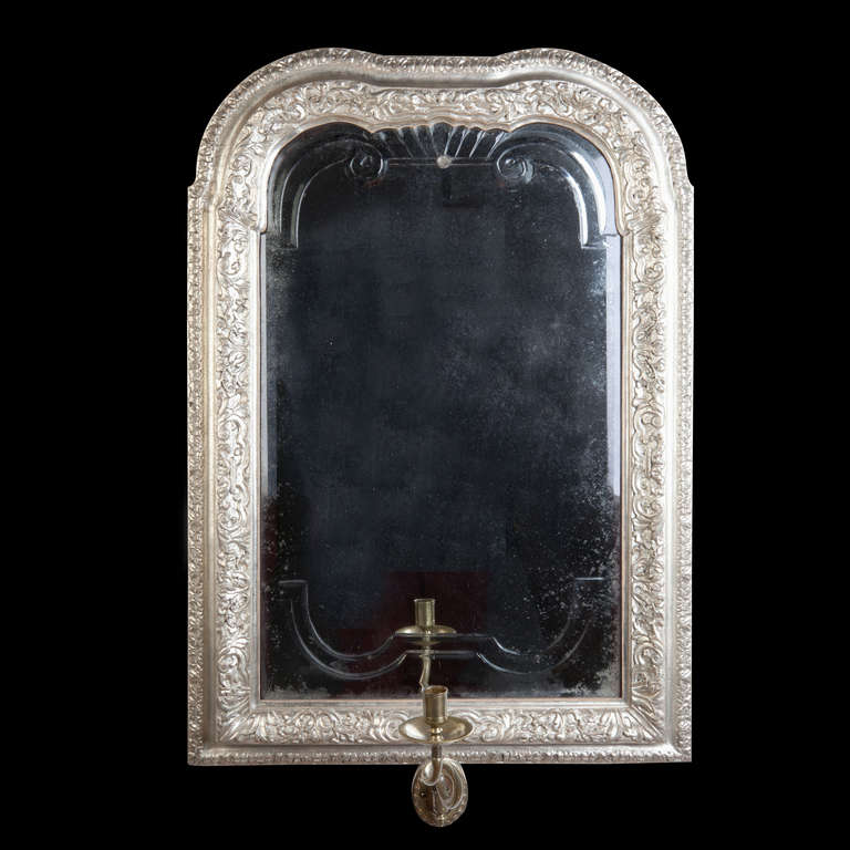A fine early 18th century Queen Anne or earlier mirror, the bevelled plate with inset architectural engraving is held in silvered collection moulded frame with profuse decoration on the surface. The sconce of later date and the silvering of later