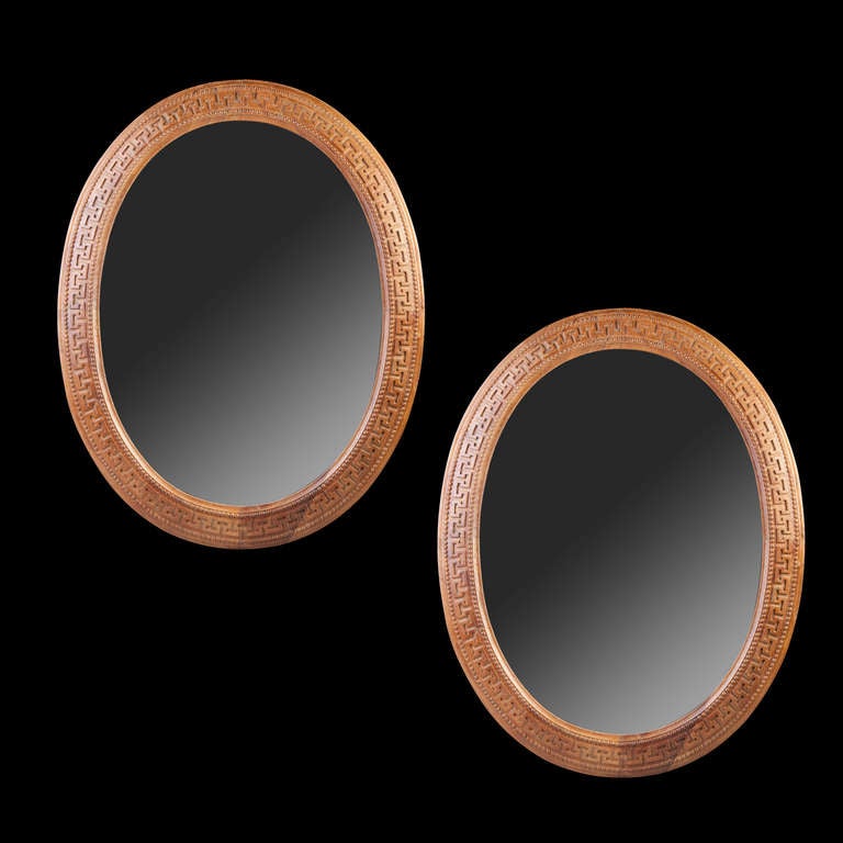 A pair of large scale oval mirrors decorated with Greek key decoration.