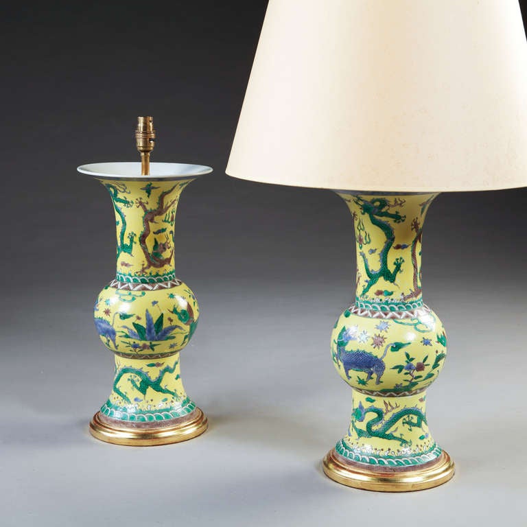 A pair of yellow glazed Chinese export baluster vases with flared bases and necks, each decorated with wucai inspired dragons and foliage. Now mounted as lamps.