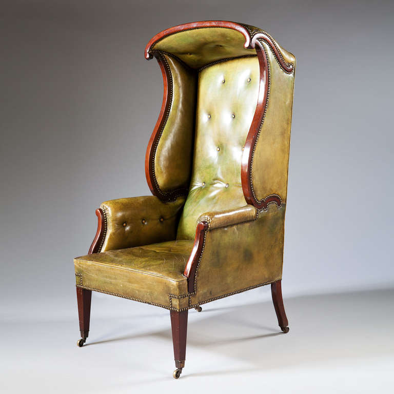 A late 19th Century Mahogany Hall Porters Chair of unusual design with a scrolled canopy and arms. Upholstered in a green leather.