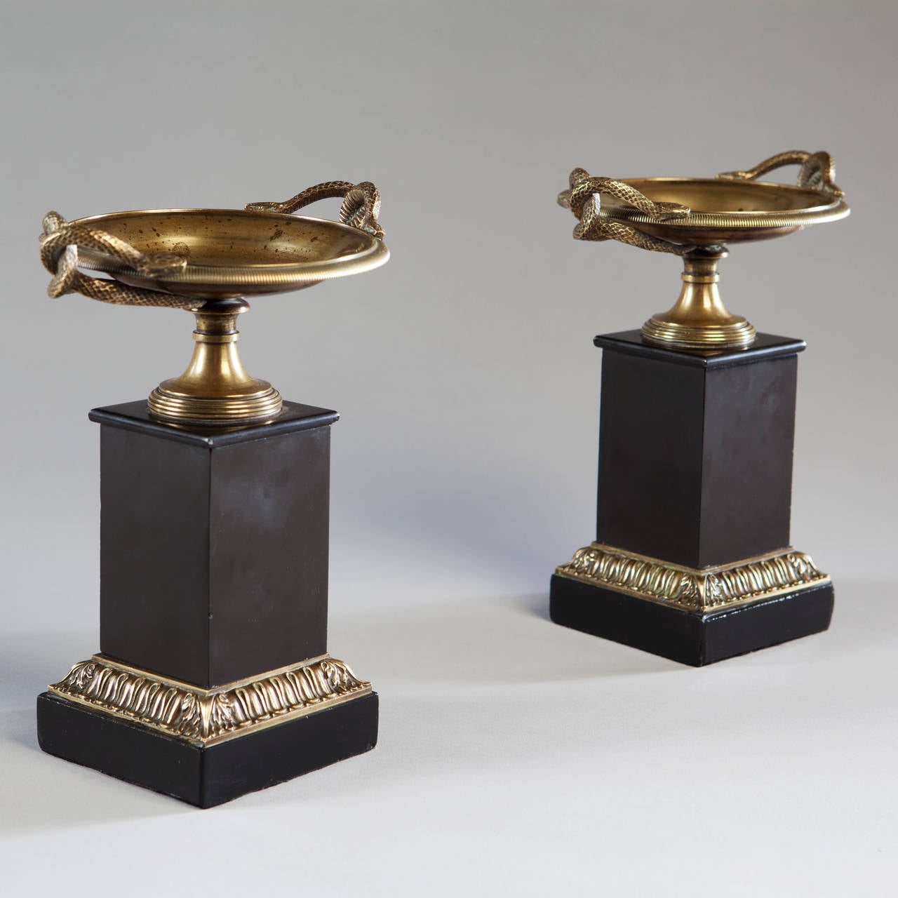 A pair of early nineteenth century bronze and black marble tazzas, the handles cast as serpents, raised on square section bronze mounted bases.