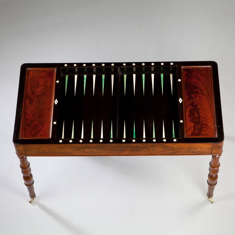 An exceptionally well figured early 19th century mahogany and ebony tric trac table with turned mahogany legs raised on brass castors, the removable top with its original black and gilt tooled leather and a suede surface for card playing, opening to