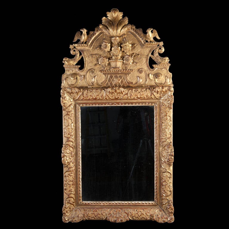 A very decorative early 18th century carved cresting of birds, flowers and dolphins supported on a fine carved, gessoed and gilt oak frame. Retaining an original early hand made mirror plate.