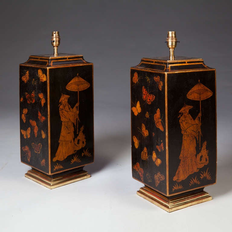 A pair of black painted four sided lamps decorated with Oriental figures and butterflies, the borders are gilt and each raised on a stepped foot.