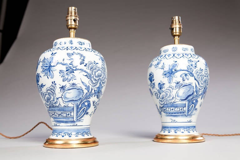 A charming pair of mid 18th century delft vases mounted as lamps. The decoration of Chinese inspiration depicting a garden scene with fret work paneling and foliage.