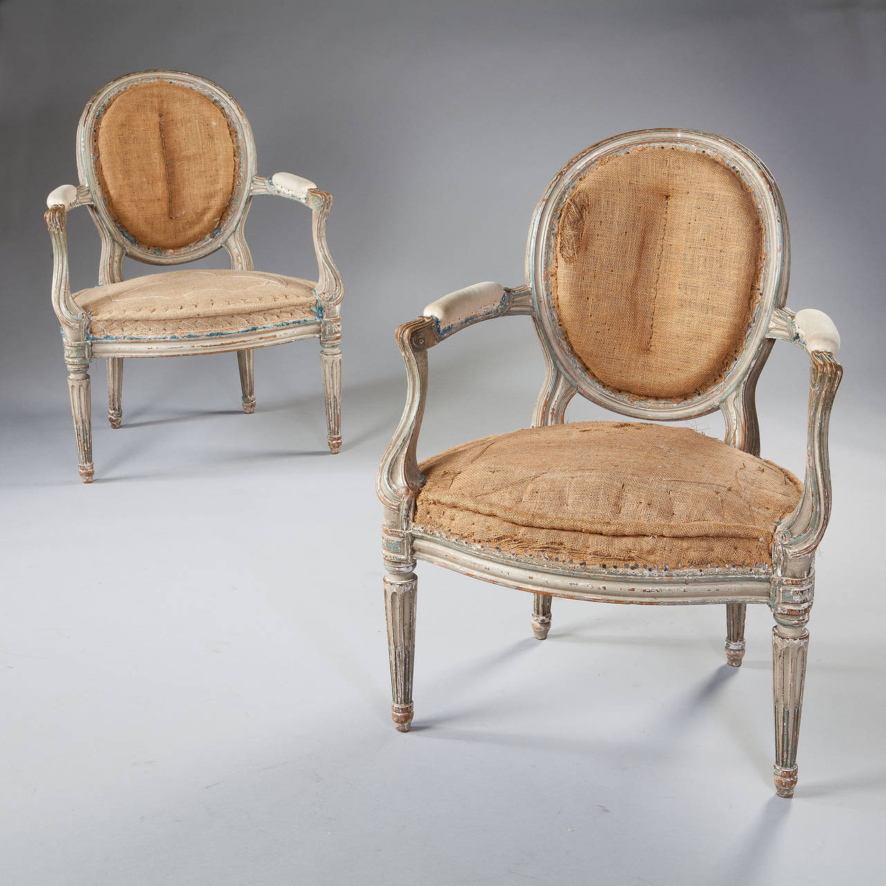 A fine pair of painted neo classical fauteuil armchairs, each with oval backs raised on elongated supports, the outswept arms curving tho the knee and raised on fluted legs with stop fluting and terminating in topie feet.