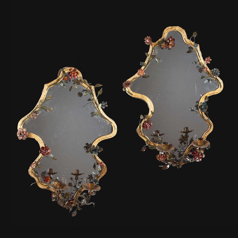 A very unusual pair of gilt Italian wall mirrors, each decorated with painted tole flowers fixed to the gilt frame and a two branch candle sconce secured at the bottom.