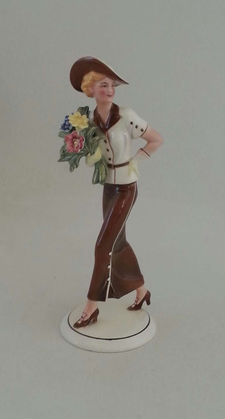 A Stunning Art Deco Figure of of a young lady with flower bouquet by Hertwig Porcelain co. 
Katzhutte Thuringia Germany. 
In a very smart brown and cream outfit with matching wide brimmed hat. 
24 cm high