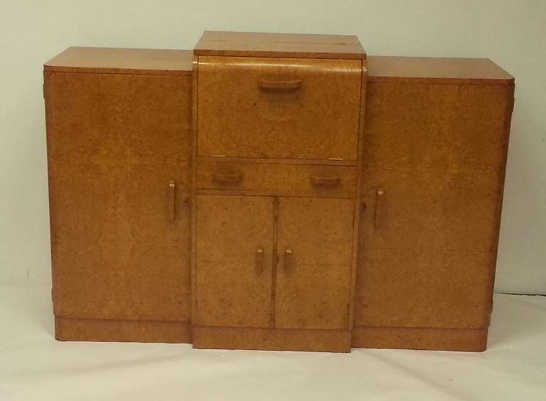 Harry and Lou Epstein (1895-1970) 
An Art Deco Birds Eye Maple Sideboard Cocktail Cabinet, the center section with drop down front to reveal mirror interior above a single drawer above cupboard fitted for bottle storage, flanked by cupboards fitted
