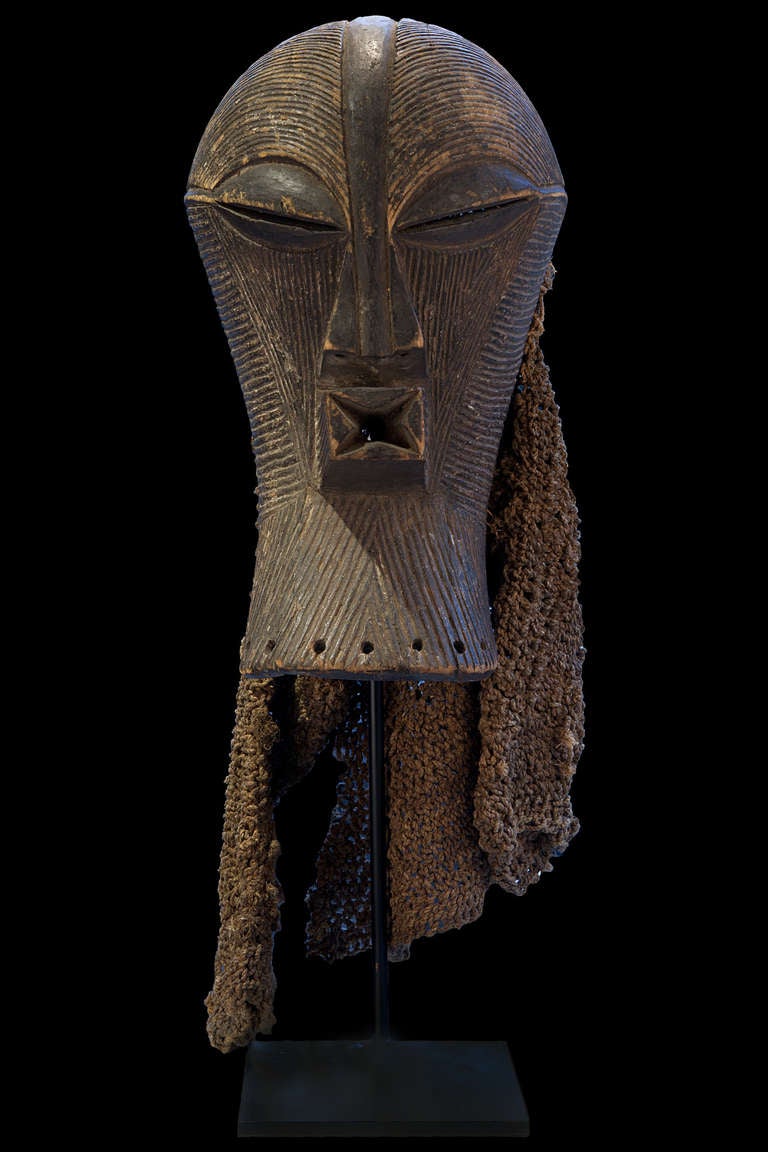 Large and elegant female Kifwebe mask with part of the original costume. Songey people, south-east Kongo.
Appears on initiations and funerals. 
Calm and introvert expression.
Nice and old patina.