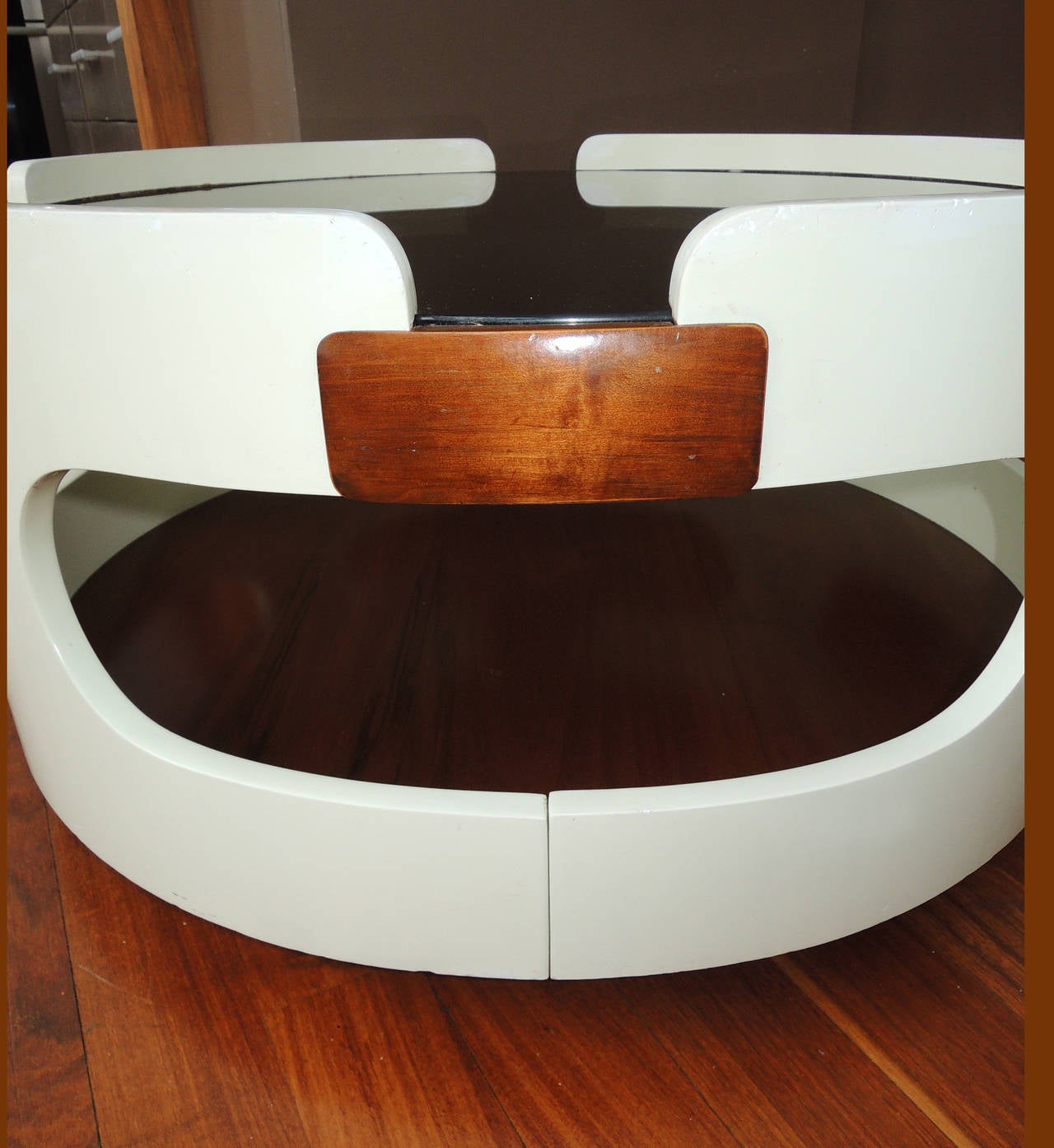 Groovy coffee table in the style of Colombo with cutouts. Lacquered curved wood, with smoked glass and mahogany. Floats on a mahogany base.