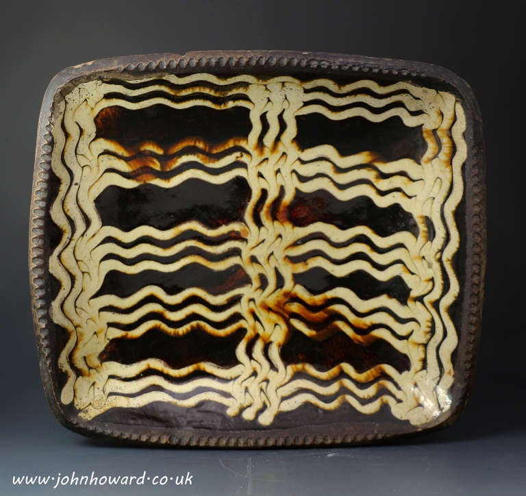 An exceptionally good late 18th century slipware baking dish, Staffordshire England.
The baking dish or loaf dish is a rounded rectangular form with 'pie crust' rim, a bold meandering line dribbled horizontally and vertically in cream slip on a