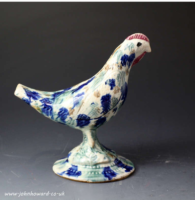 Antique pottery figure of a bird in the form of a money box bank.
The figure is naively modelled and decorated in underglaze colours with a profusion of blues and browns. The wattle of the bird is coulered red maroon a very distinctive feature of