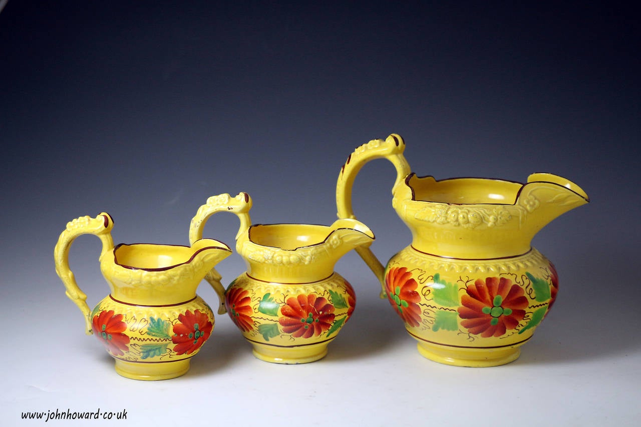 A fine set of three Staffordshire pottery graduated size pitchers with a canary yellow ground and decorated with bright flowers and leaves in enamel colours. 
Rare to locate an original set of three from the early 19th century especially in extra