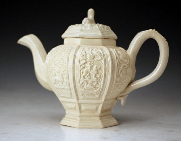 Antique saltglaze stoneware teapot with relief decorated panels the cover with a figure of an animal as a finial.
One of the early examples from the Staffordshire potters in the mid 18th century.
The baluster shaped pot has eight vertical panels