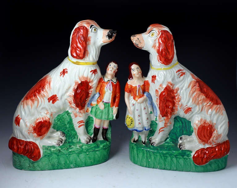 Agood pair of antiques Staffordshire pottery figures of Afghan dogs modelled seated on a bright green base. The adition of diminutive children provides a comedy to this charming decorative pair. 
Staffordshire.