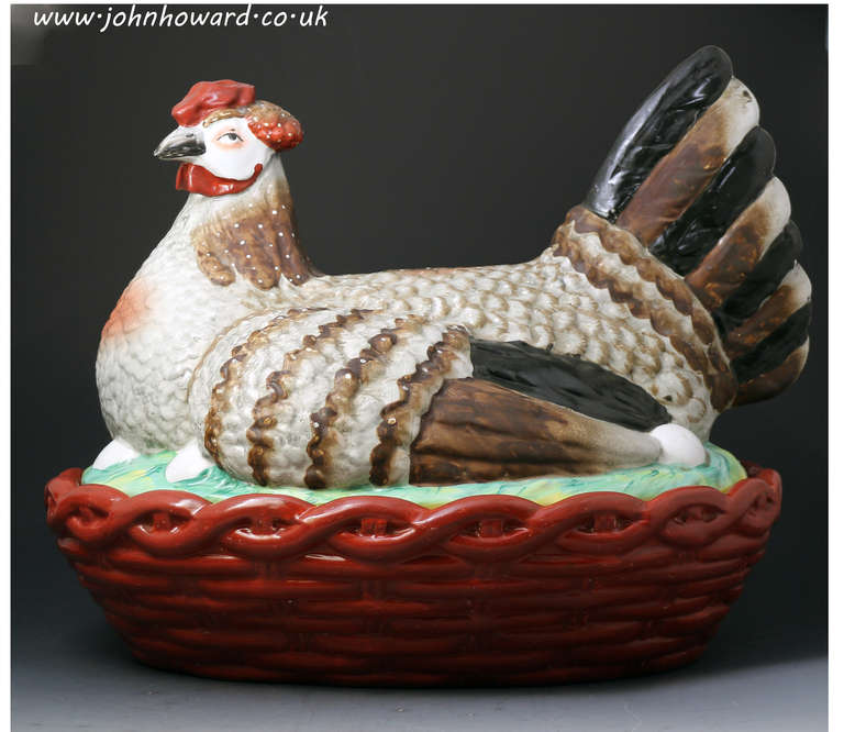 A massive Staffordshire pottery covered tureen in the figure of a hen seated on a basket type nest. The basket is a burnt orange whilst the hen is naturally decorated in soft grey and brown hues with red highlights
This is the largest 