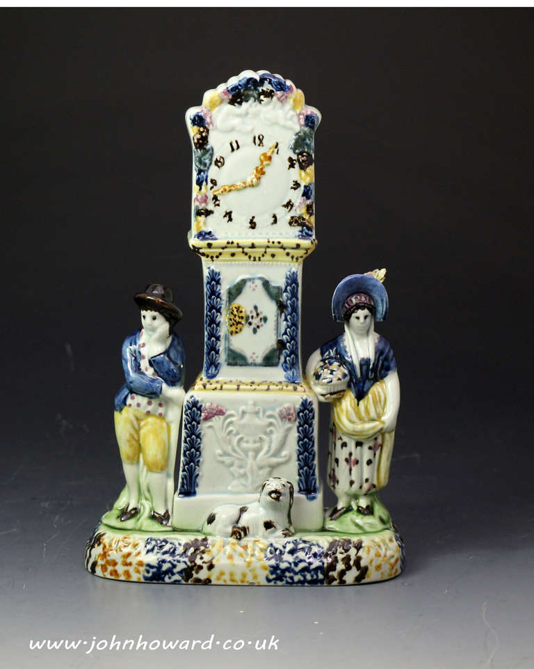 Antique English prattware clock figure money box from Yorkshire in the early 19th century period.
The piece is modelled with a central longcase clock and flanked by figures of a lady with a great hat and a rather weary looking farmer. The figure of