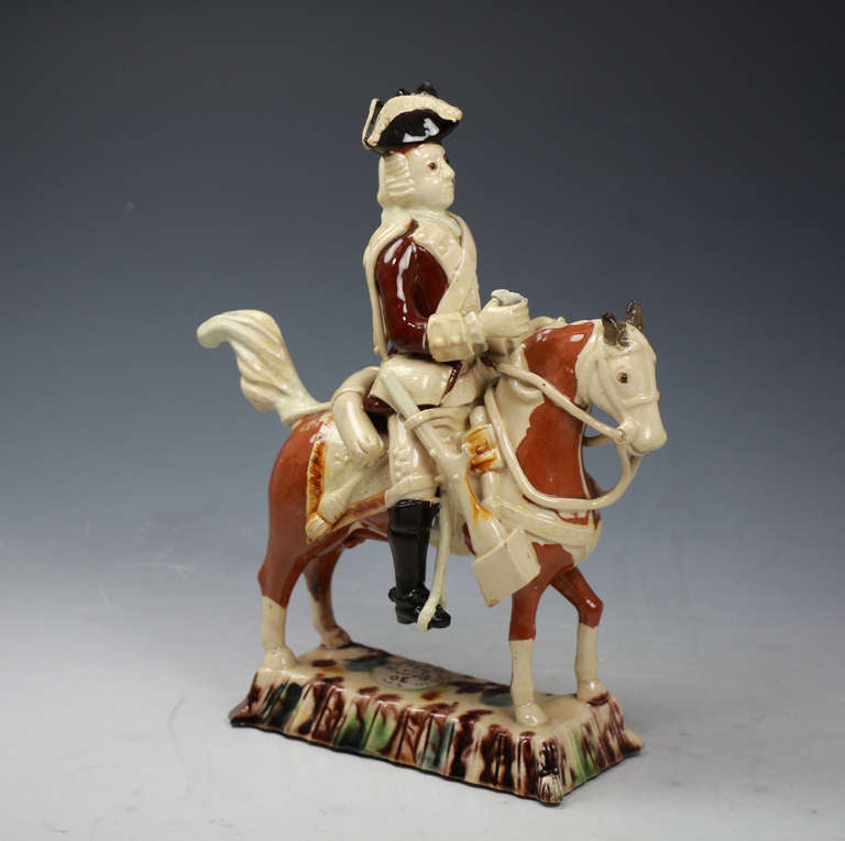 
Staffordshire Creamware pottery Equestrian figure of a mounted officer of Astbury-Whieldon type.

The officer modelled holding the reigns,wearing a tricorn hat and a jacket edged in a cream slip. His breeches are cream coloured and he sports