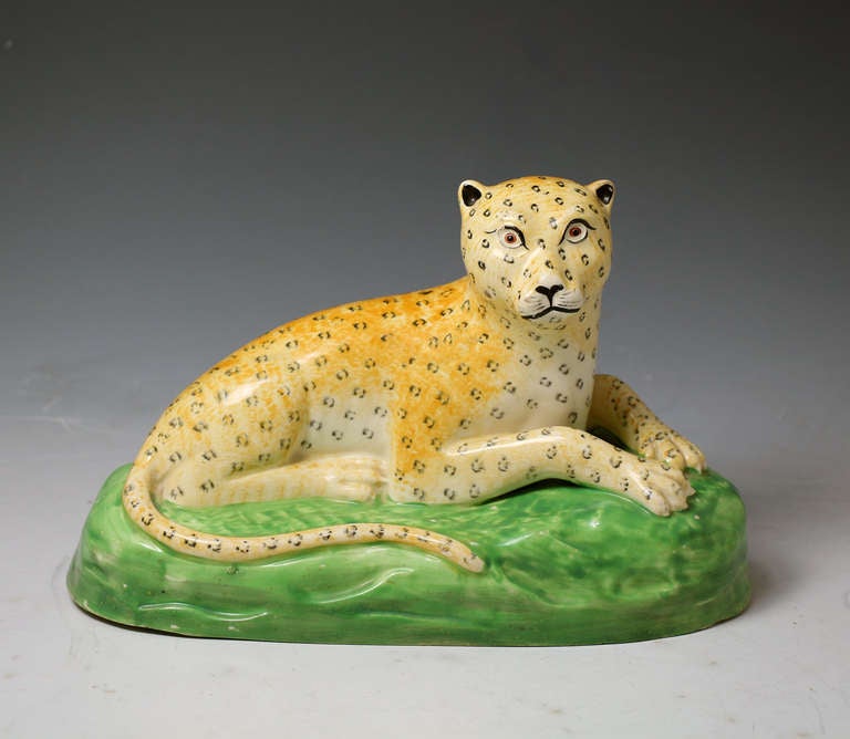 A rare antique Staffordshire creamware pottery of a reclining leopard on a green base. 
The modelling and colouring are of the best quality.One of the best figures produced by the Staffordshire potters depicting wild animals. 

Literature: Weldon